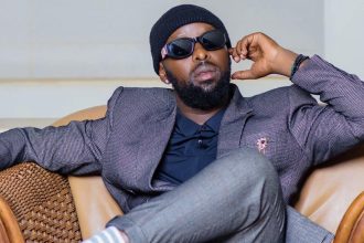 Eddy Kenzo in a stylish suit and shades, relaxing on a couch.
