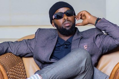 Eddy Kenzo in a stylish suit and shades, relaxing on a couch.