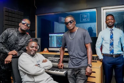 King Saha, Bobi Wine, and Nubian Li recording music together at Audio One studio, seated around a mixing console with headphones and microphones.